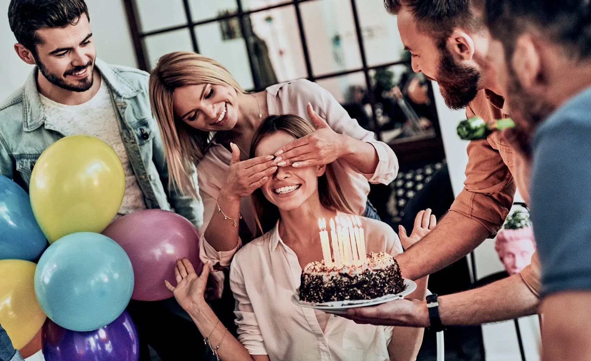 Friends organizing a surprise birthday party with cake and colorful balloons (source: www.smartbox.com)
